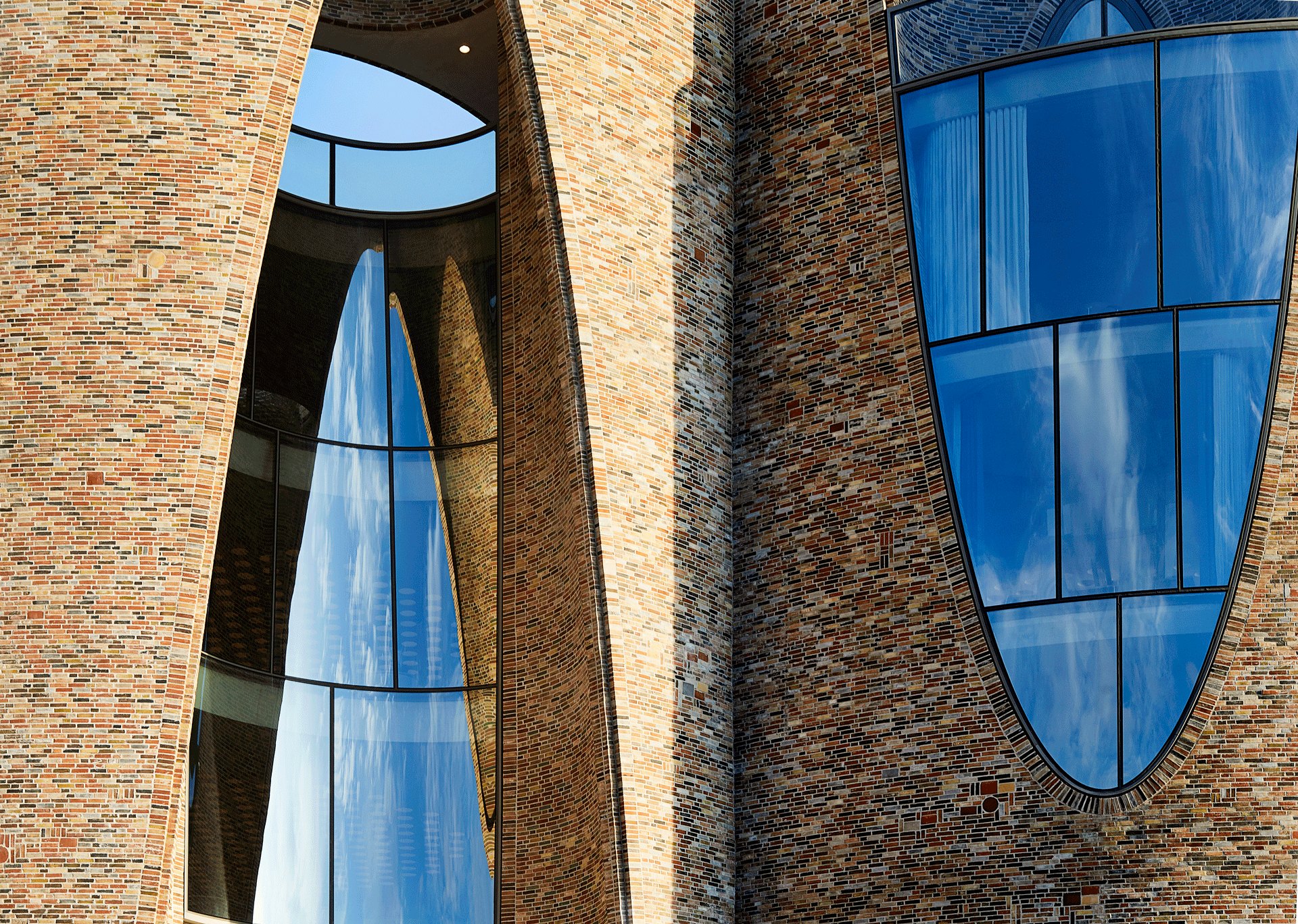 Nærbillede af broget murstensfacade med buede glasvinduer, der spejler himlen
