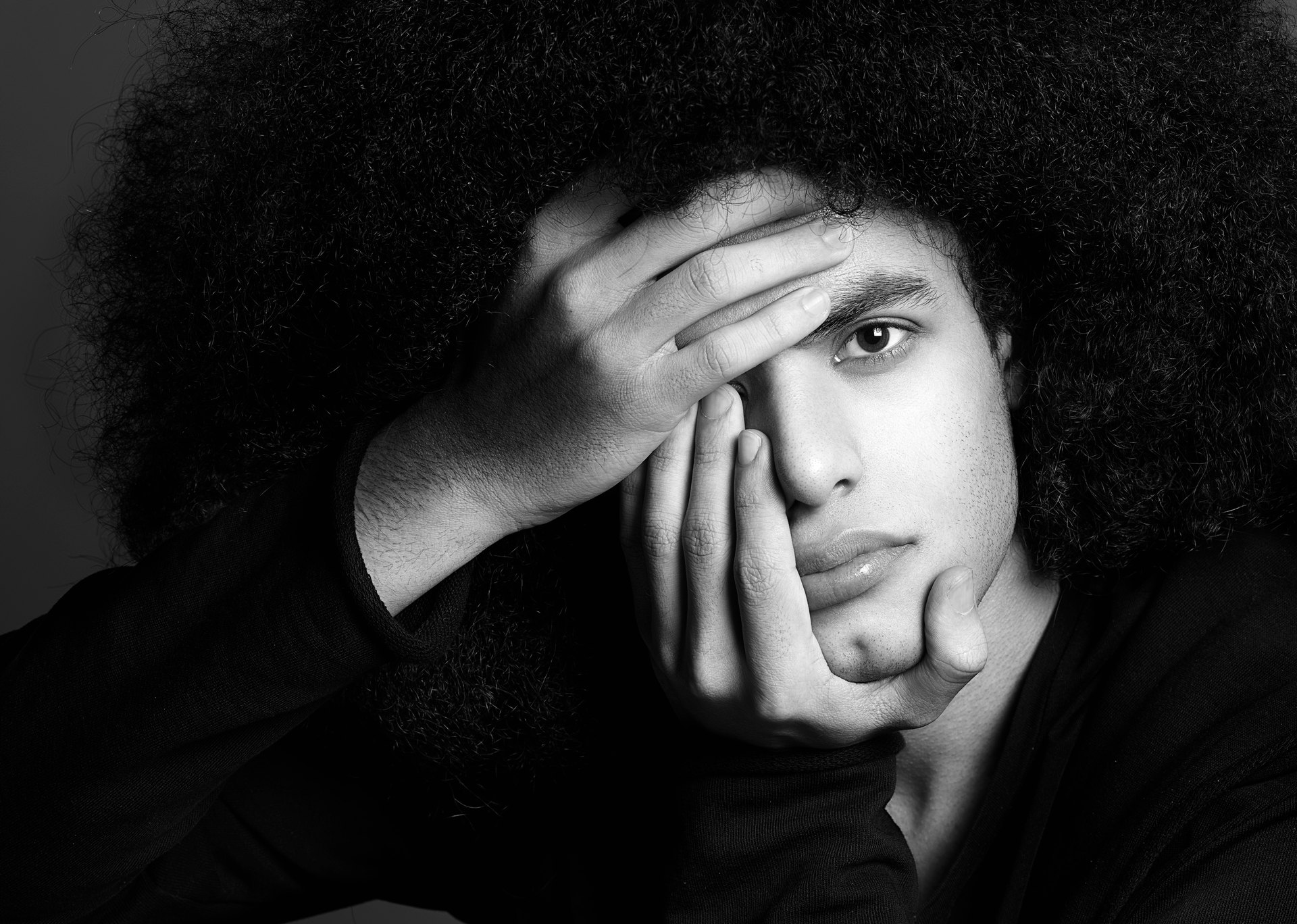 Sort-hvidt fine art-portræt af mand med voluminøs afro, hånden ført op over ansigtet